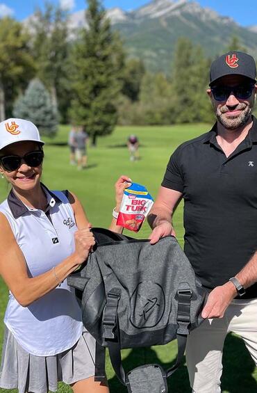 Man and woman posing on a golf course, holding up a package of Big Turks candy.