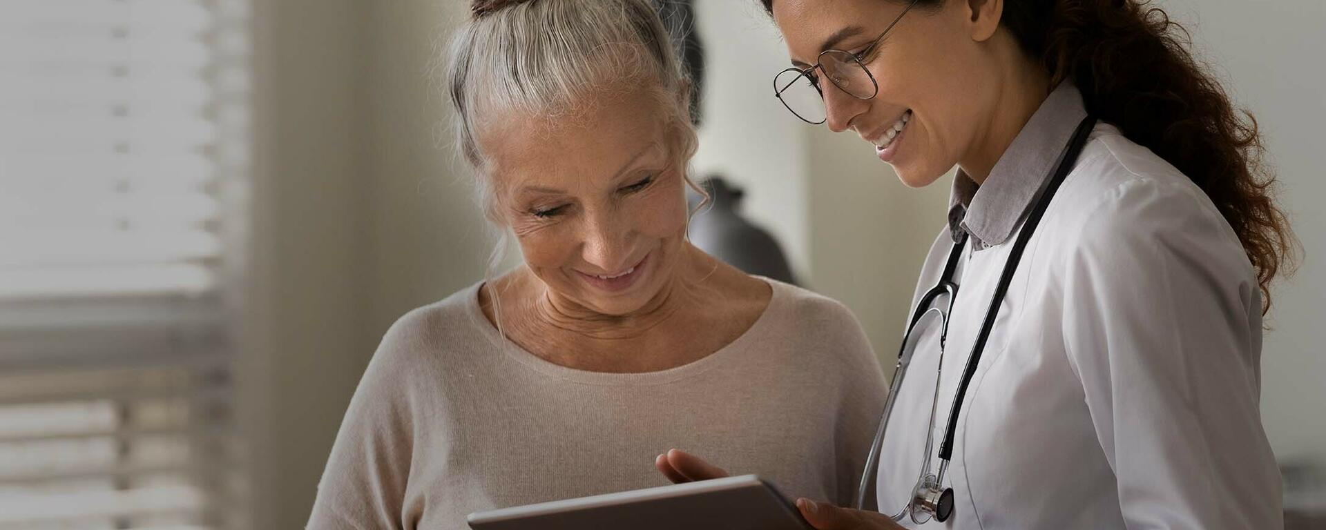 A doctor stands beside a patient, pointing to a tablet.