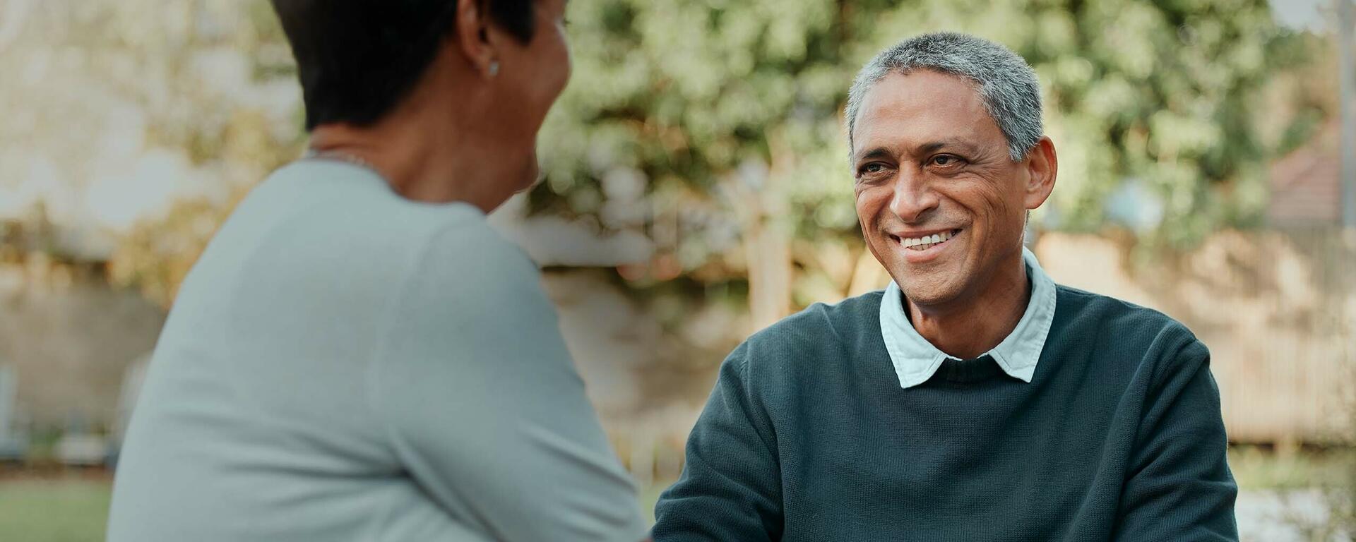 A senior man and woman gaze at each other, while smiling and talking.