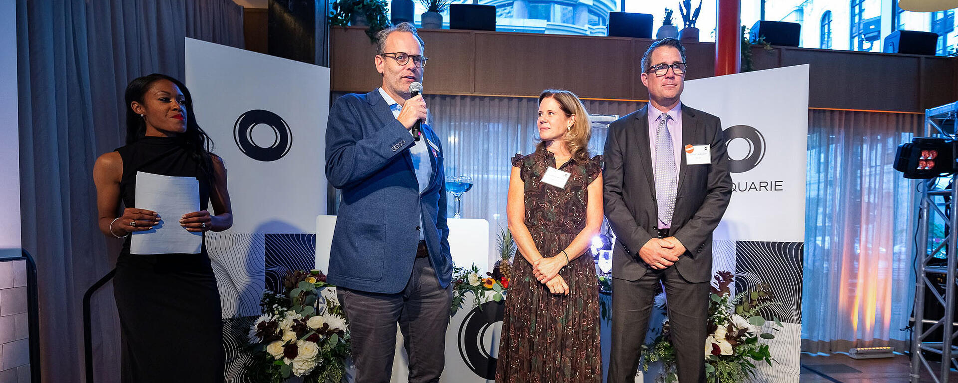 Aarnoud van Weelderen presenting from a stage at the The Macquarie Mix-Off event, with Lindsey McKay and Trevor Johnson beside him.