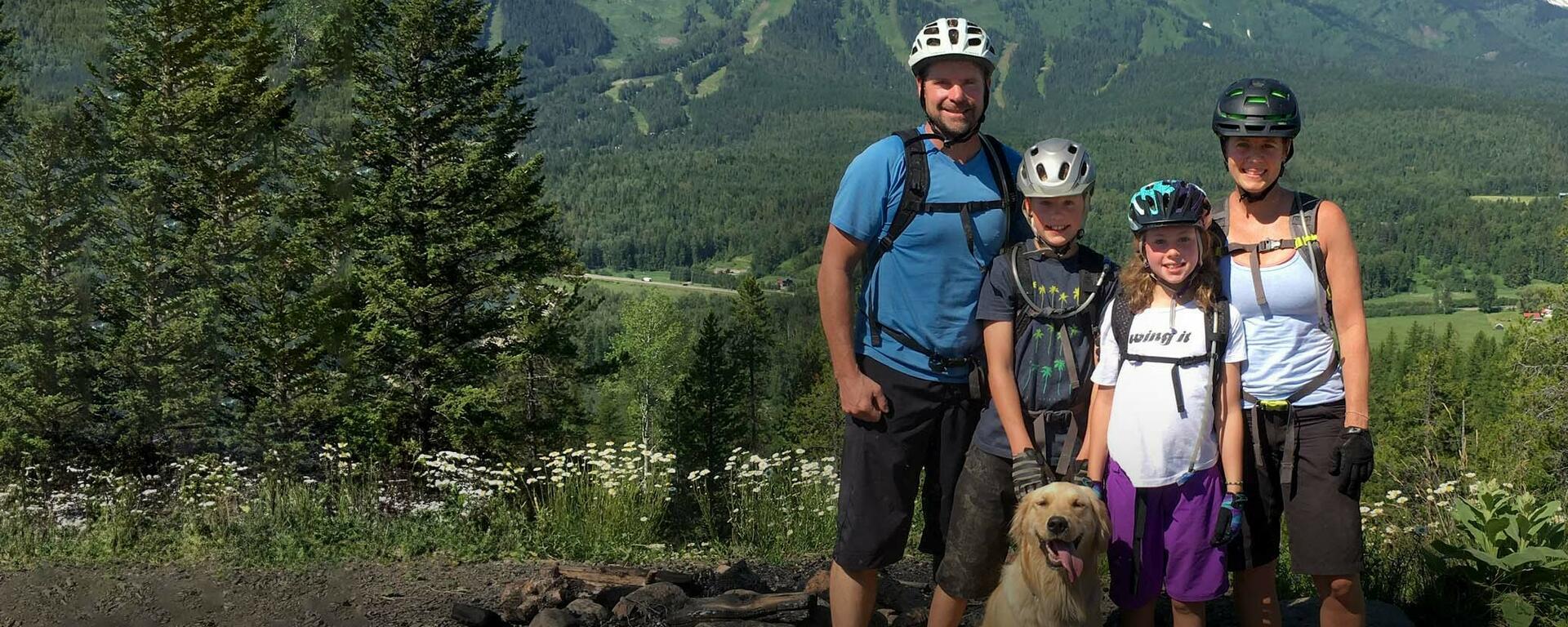 Mike McClay standing with his wife, two young kids and dog in front of a forest and mountains.