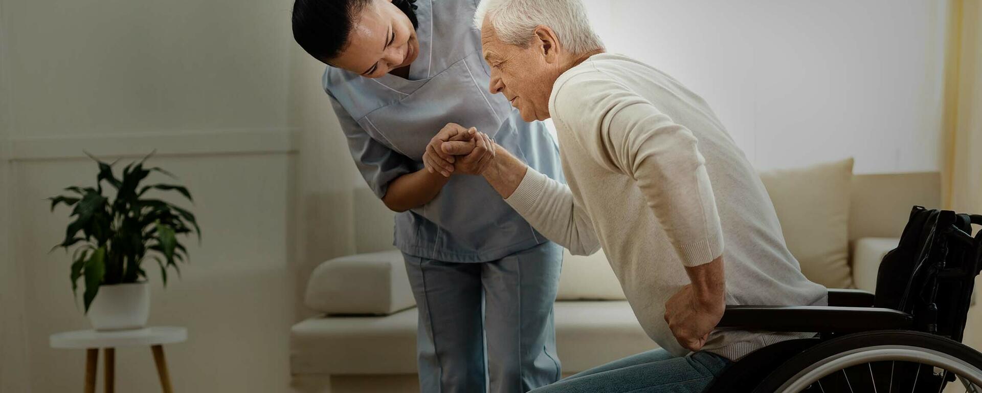 Nurse helps a senior man out of his wheelchair.