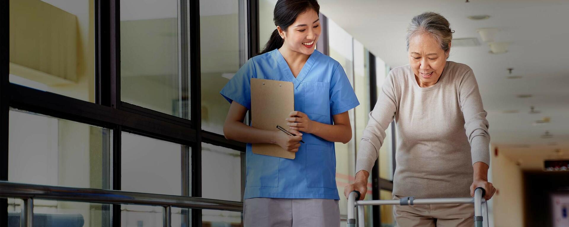 A nurse walks beside a senior woman who is using a walker.