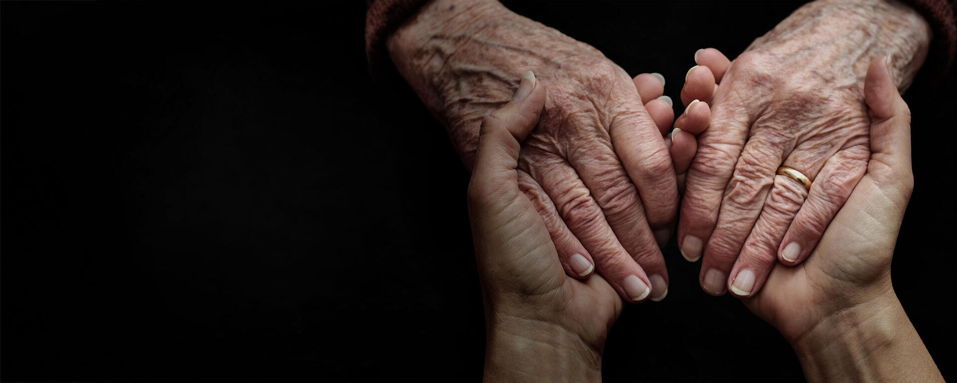 Two hands reach in to hold a senior woman's hands in a comforting and supportive way.