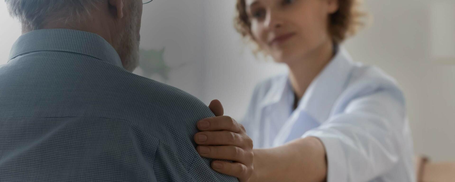 A woman puts her hand on a senior man's arm to comfort him.