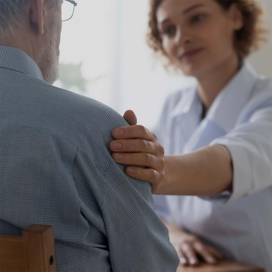 A woman puts her hand on a senior man's arm to comfort him.