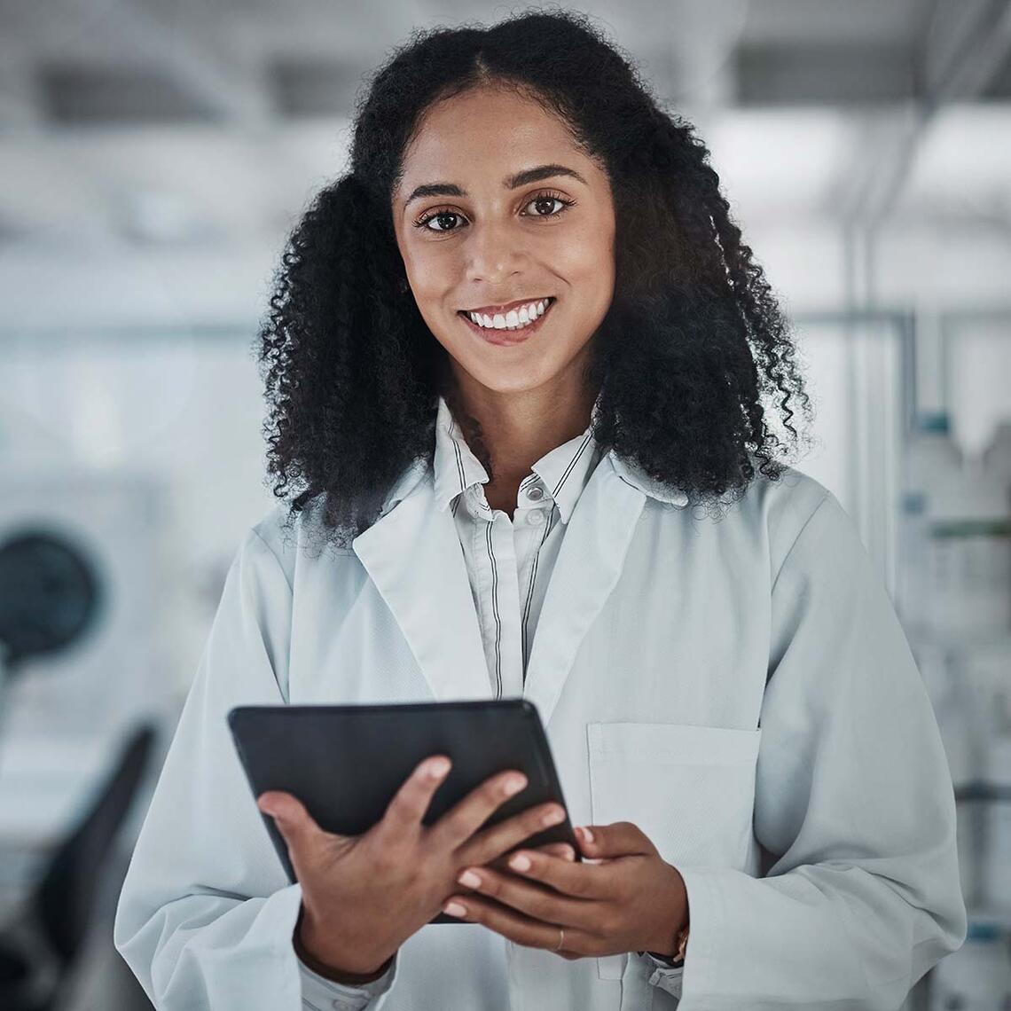 A woman in a lab coat smiles as she poses in a lab.