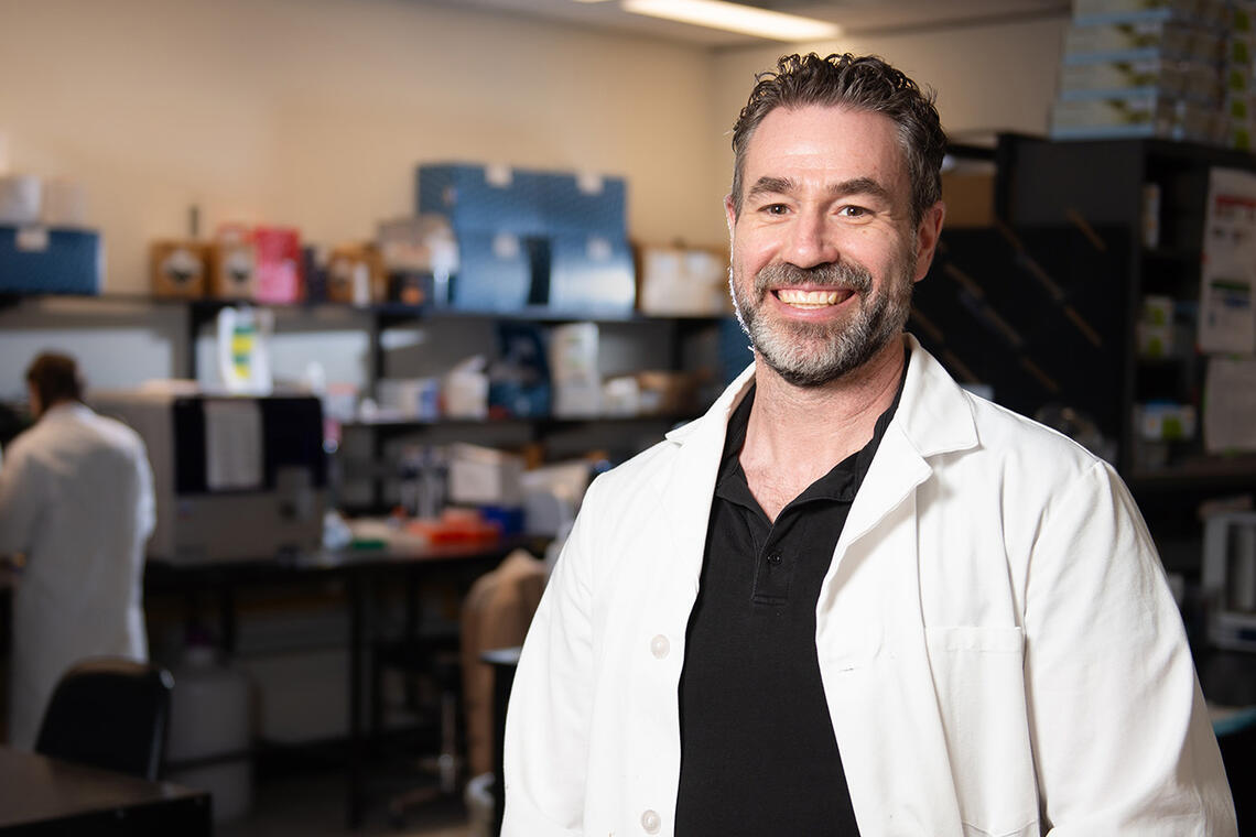 Dr. Matthew Hill stands in the foreground with his lab in the background.
