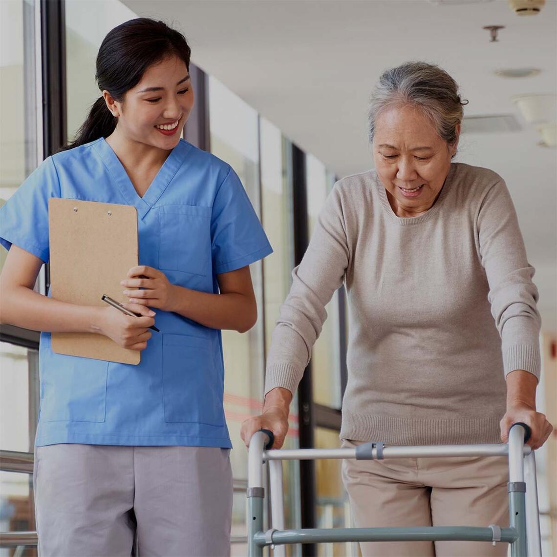 A nurse walks beside a senior woman who is using a walker.