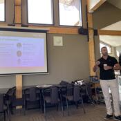 Dr. Matthew Hill PhD presenting at the front of a room.