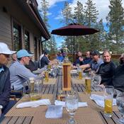 A large group of people sitting at an outdoor table, enjoying glasses of beer.