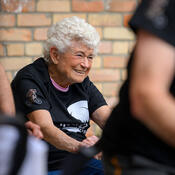 A senior woman is wearing a Hustle with Hunt t-shirt, riding a spin bike.