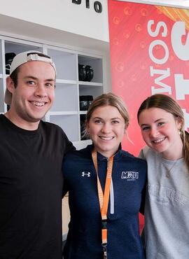 One man and two women stand side-by-side, posing in front of a University of Calgary vertical banner.
