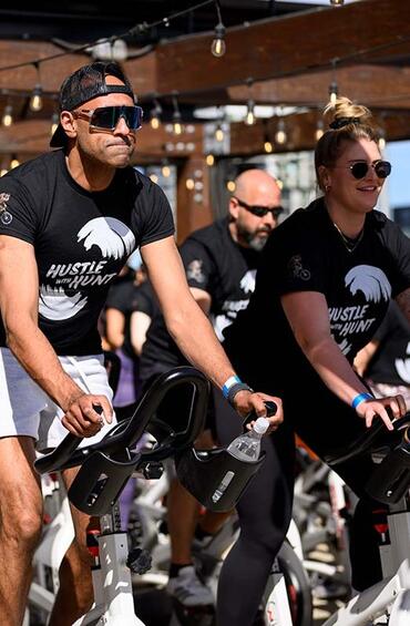 A group of people on spin bikes, wearing Hustle with Hunt t-shirts.