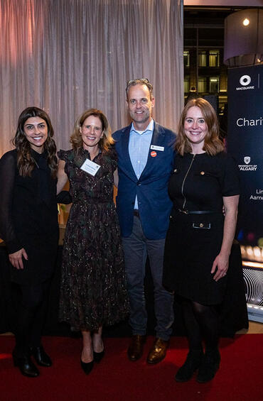 Four people stand side-by-side, posing for the camera, with a sign behind that reads “7th Annual Charity Fundraiser Mix-off.”