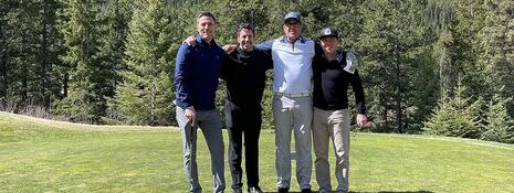 Four people posed on a golf course, standing in front of a trophy.