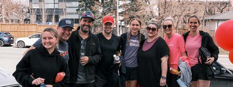Eight people stand side-by-side outside, posing in workout clothes.