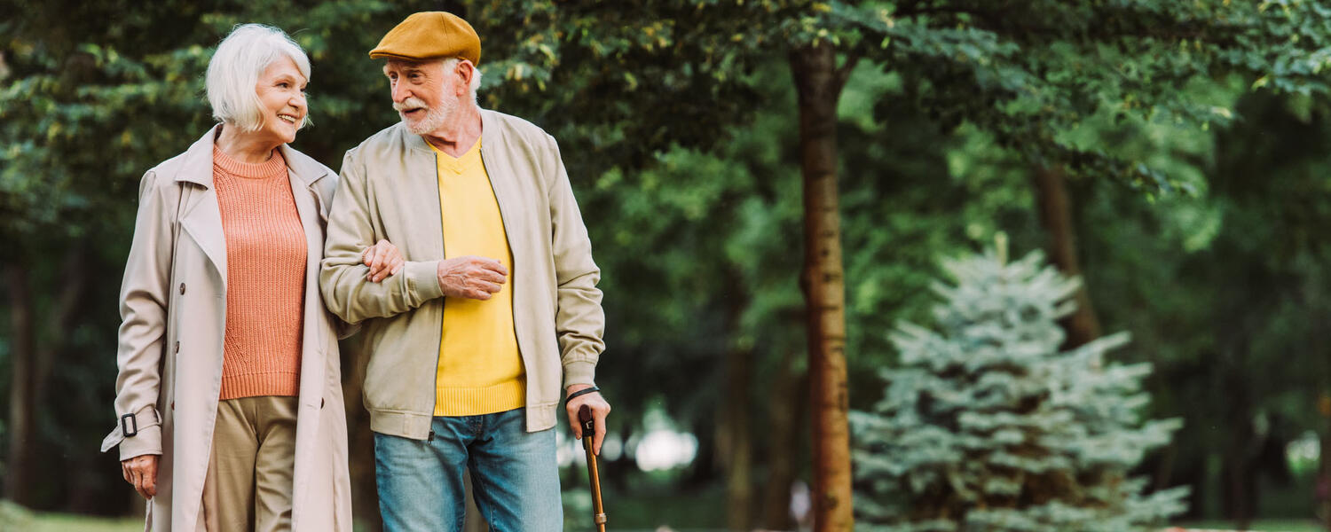 A senior man and woman walk outside, arm in arm, smiling and talking.