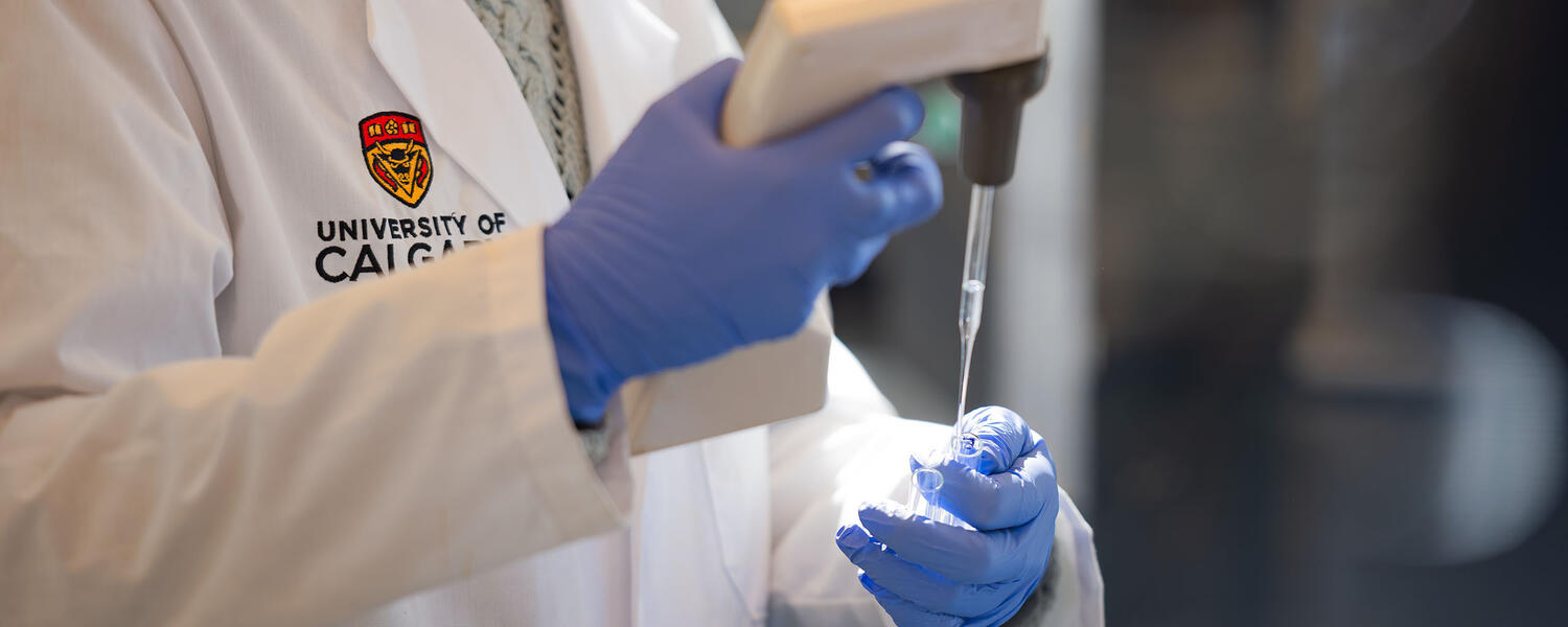 A researcher is working in a lab, wearing a University of Calgary lab coat.