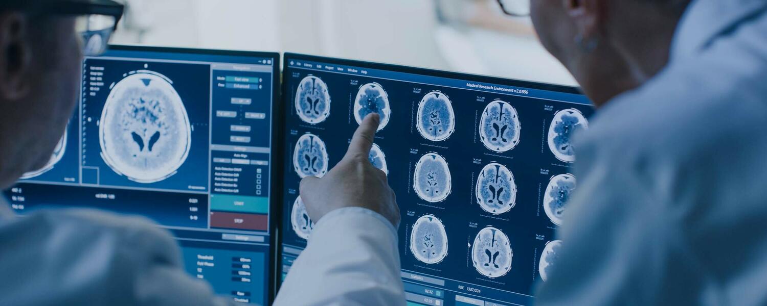 Two doctors are reviewing brain MRI scans on computer screens.