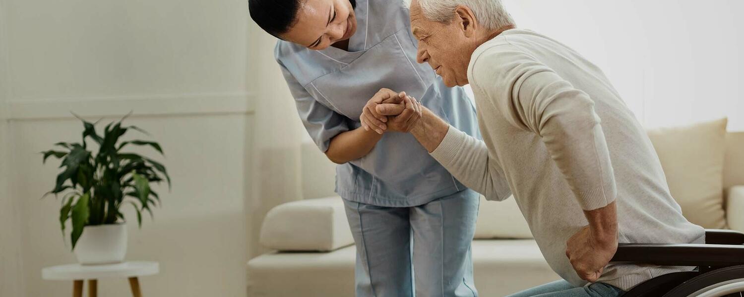 A nurse helps a senior man out of his wheelchair.