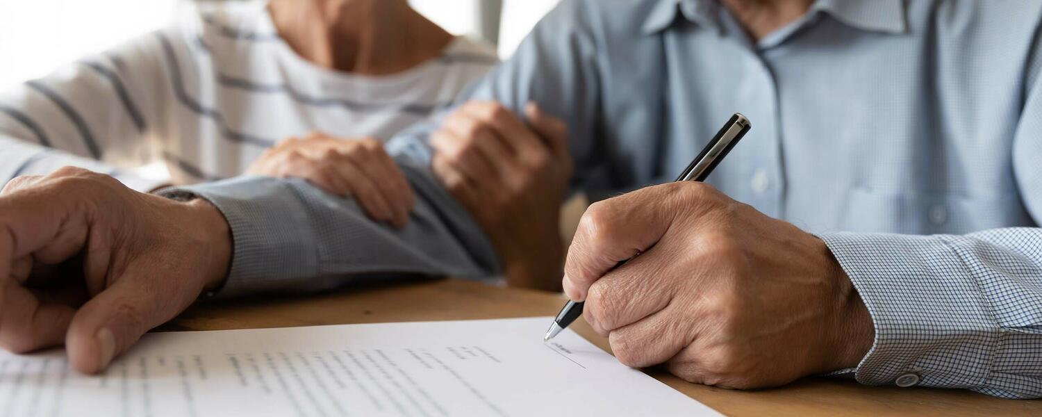 A senior couple sits together signing documents.