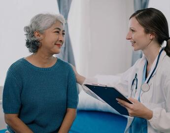 A doctor puts her hand on her senior patient's shoulder in a comforting way.