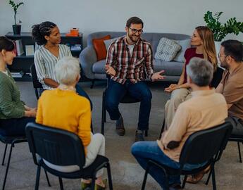 A group of seven people are sitting in chairs in a circle, and talking. 